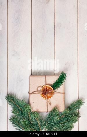 Confezione regalo in stile eco-friendly: Carta naturale ruvida, corda di iuta, ramoscelli di abete rosso su sfondo di legno bianco. Foto Stock