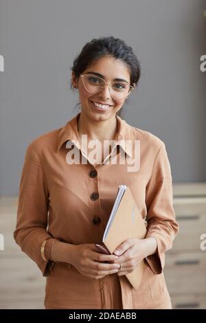 Ritratto di giovane donna d'affari riuscita in occhiali sorridenti a macchina fotografica mentre si è in ufficio Foto Stock