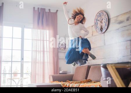 Stile di vita gioioso e concetto di successo per le donne - donna saltando sul divano per la felicità - allegro positivo giovane caucasica signora godere la nuova vita con un salto Foto Stock