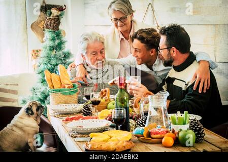 Allegra famiglia caucasica godere e celebrare insieme a casa con tabella piena di decorazioni natalizie - età e generazioni miste dai teenager agli anziani e agli adulti si divertono Foto Stock