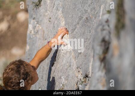 Primo piano della mano di una giovane donna che tiene sulla pietra durante l'arrampicata Foto Stock