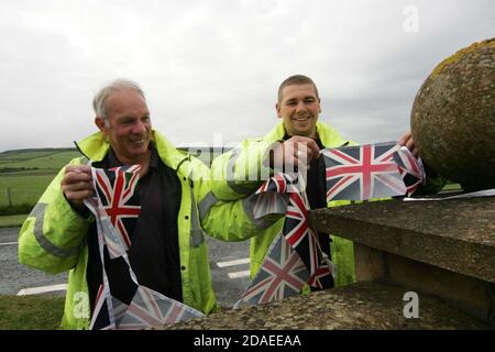 Ayrshire, Scozia, Regno Unito. La torcia olimpica di Londra 2012 viaggia attraverso l'Ayrshire del Sud, allietato dalle comunità locali e dai bambini della scuola. Due lavoratori in alto visabitly jackeets appendere Union Jack , Union Flag Bunting Foto Stock