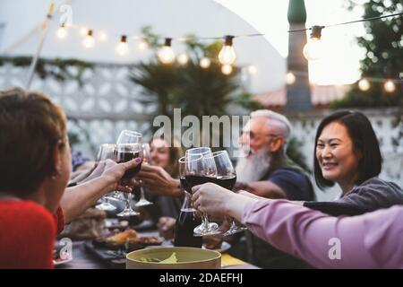 Cena in famiglia e degustazione di bicchieri di vino rosso in barbecue cena festa - persone con età ed etnia diverse divertirsi insieme Foto Stock