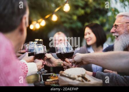 Cena in famiglia e degustazione di bicchieri di vino rosso in barbecue cena festa - persone con età ed etnia diverse divertirsi insieme Foto Stock