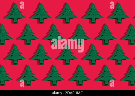 Alberi decorativi di Natale su superficie rossa. Oggetto modello di feltro vacanza albero con ombra. Carta da parati natalizia alla moda. Biglietto d'auguri per le festività Foto Stock