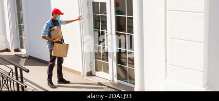 addetto alla consegna in maschera protettiva vicino alla casa del cliente, all'aperto Foto Stock