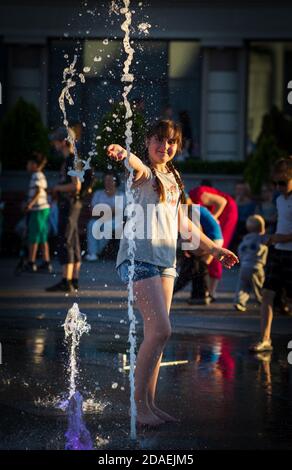 KIEV, UCRAINA - 05 giu 2018: Ragazza allegra e felice che gioca in una fontana d'acqua e godendo i flussi freddi di acqua in una giornata calda. Estate calda. Foto Stock