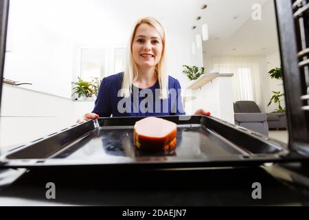 Ritratto di una giovane donna che prepara il cibo in cucina. La giovane casalinga sta tenendo la carne appena sfornata Foto Stock