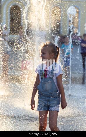 KIEV, UCRAINA - 05 giu 2018: Ragazza allegra e felice che gioca in una fontana d'acqua e godendo i flussi freddi di acqua in una giornata calda. Estate calda. Foto Stock