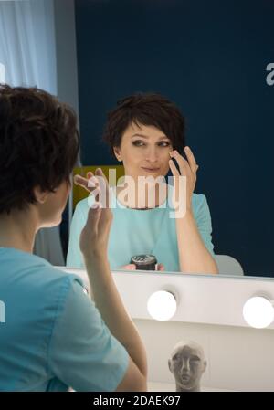 riflessione nello specchio di una donna che applica la crema sul viso Foto Stock