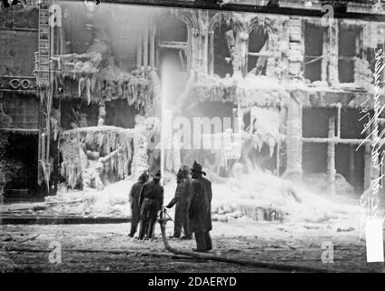 Immagine di cinque vigili del fuoco che spruzzano acqua sul Colby Furniture Store che è coperto di ghiaccio da incendio estinguente, Chicago, Illinois. Foto Stock