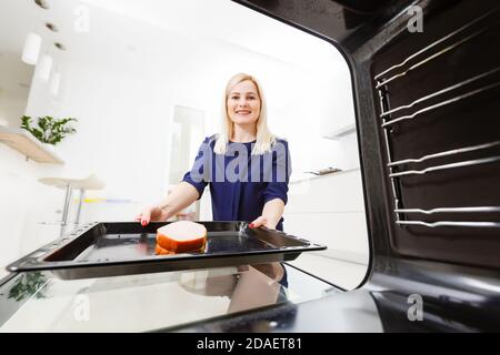 Ritratto di una giovane donna che prepara il cibo in cucina. La giovane casalinga sta tenendo la carne appena sfornata Foto Stock