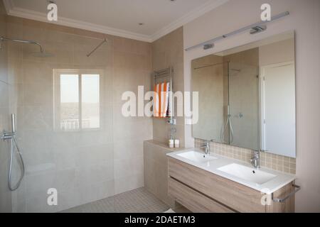 Bagno interno con grande doccia piastrellata e doppio lavabo con specchio Foto Stock