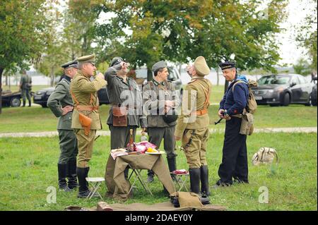 I reenattori vestiti in uniformi di ufficiali tedeschi della seconda guerra mondiale e ufficiali russi della prima guerra mondiale che bevono vodka su un prato. 4 ottobre 2012. Kiev, Foto Stock