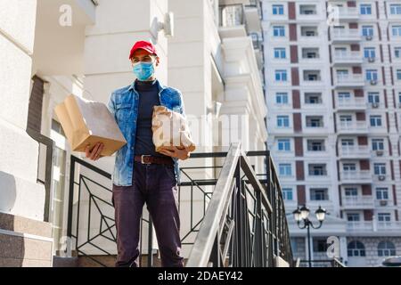 uomo per la consegna di cibo con sacchetti in una maschera protettiva il suo volto Foto Stock