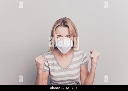 Primo piano ritratto di una donna furiosa che mostra pugni che indossano il bianco maschera facciale isolata su sfondo grigio Foto Stock