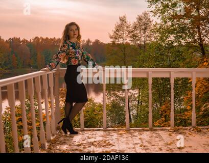 Una donna allegra si appoggia contro una ringhiera bianca adulto con un aspetto carismatico biondo in una camicia colorata funziona su un computer su Foto Stock