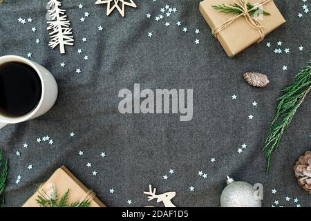 Decorazioni natalizie in legno con rami sempreverdi, fiocchi di neve, tazza da caffè e regali su plaid grigio. Disposizione piatta, vista dall'alto. Foto Stock