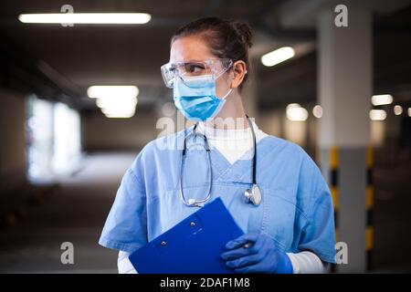 Medico di UTI femminile nel parcheggio dell'ospedale, tasto di prima risposta medico lavoratore, tenendo appunti scheda medica paziente, guardando via, emergenza s. Foto Stock