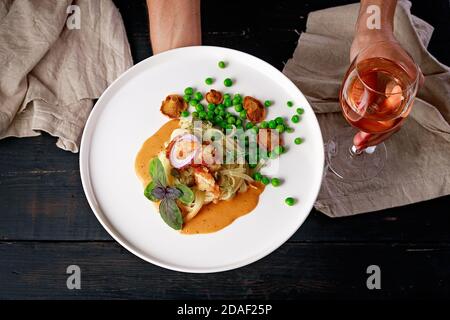 Pasta e gamberetti fritti con piselli verdi e salsa originale di chanterelle e un bicchiere di vino rosato su uno sfondo scuro. Vista dall'alto Foto Stock