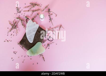 Strumenti di massaggio rosa e verde Gua Sha realizzati in quarzo rosa su sfondo rosa con fiori di lavanda essiccati. Concetto di bellezza. Concetto Flatlay Foto Stock