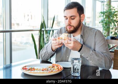 Affamato uomo caucasico mangiare pizza italiana in pizzeria. Deliziosa pizza al caffè. Foto Stock