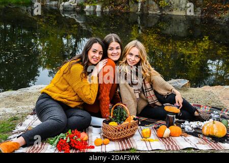 Tre donne migliori amici al picnic autunno nel parco. Plaid colorato, thermos e pompine. Amici divertirsi all'aperto. Foto Stock