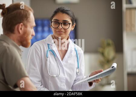 Giovane dottoressa in occhiali con ricetta medica in lei mano e parlare con il suo paziente in ospedale Foto Stock
