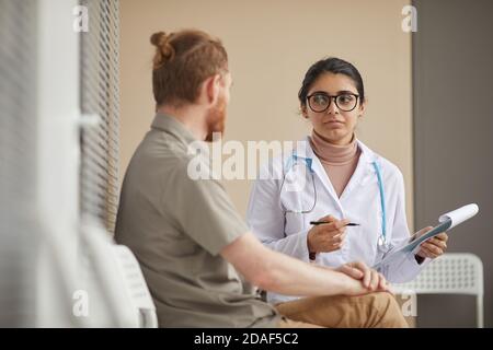 Giovane dottoressa che tiene la scheda medica e discute con il paziente la sua malattia mentre si siedono in corridoio Foto Stock