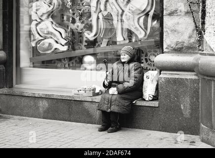 Kiev, Ucraina - 16 novembre 2019: Persone svantaggiate e impoverite sulla strada di Kiev. Una donna anziana si siede vicino a una vetrina e vende noci e. Foto Stock