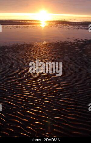 Ayr, Ayrshire, Scozia, Regno Unito. Sole che sorge sopra l'isola di Arran come vista rom Ayr Beach con sabbia bagnata come la marea si spegne Foto Stock