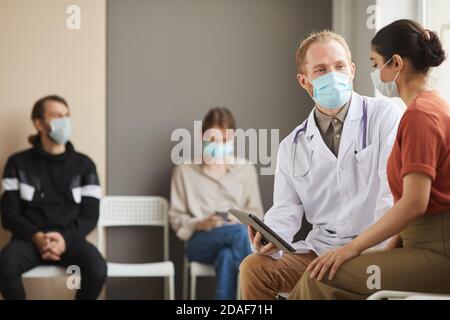 Medico di sesso maschile utilizzando PC tablet e parlando con la donna a. il corridoio dell'ospedale con altre persone sullo sfondo Foto Stock