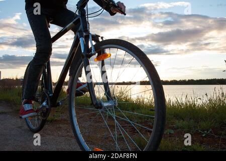 Ruota di una bicicletta in movimento sullo sfondo del lago e il sole che tramonta. Foto Stock