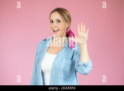 Ritratto di una giovane donna seria in piedi con la mano distesa mostra il movimento di arresto isolato su sfondo rosa Foto Stock