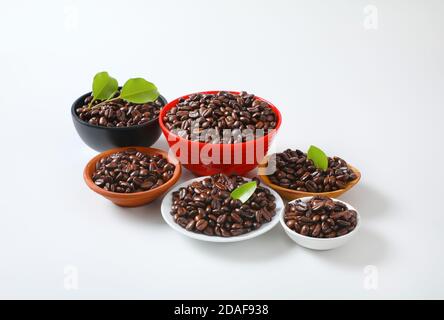 Chicchi di caffè tostati in vari recipienti e sul piatto Foto Stock