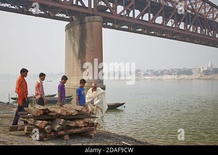 Varanasi, India, dicembre 2015. Gli uomini preparano una pira funeraria vicino ad un ponte in un ghat sul fiume Gange. Foto Stock