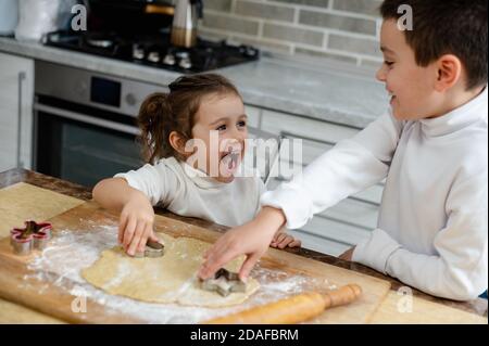 I bambini cucinano i biscotti di Natale e ridono a vicenda. Foto Stock