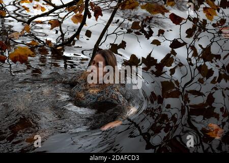 Donna che indossa un abito, all'interno dell'acqua in un giorno d'autunno Foto Stock