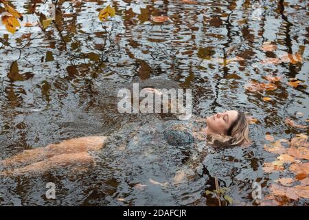 Donna che indossa un abito, all'interno dell'acqua in un giorno d'autunno Foto Stock