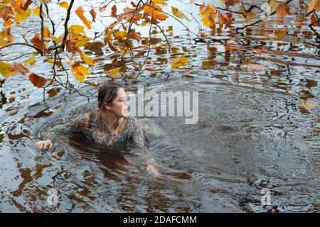 Donna che indossa un abito, all'interno dell'acqua in un giorno d'autunno Foto Stock