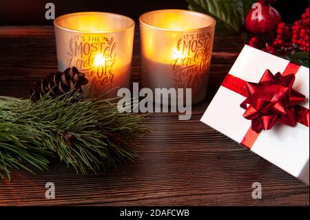 Composizione di Capodanno. Regalo in una scatola bianca con un casco, accanto a due candele di Natale e rami di un albero di Natale. Foto Stock