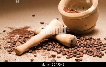 mortaio e pestello in legno, con chicchi di caffè naturale e polvere macinata, su tela di rafia e fondo marrone Foto Stock