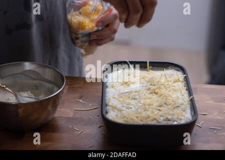 Preparazione delle lasagne, versando a mano il formaggio grattugiato Foto Stock