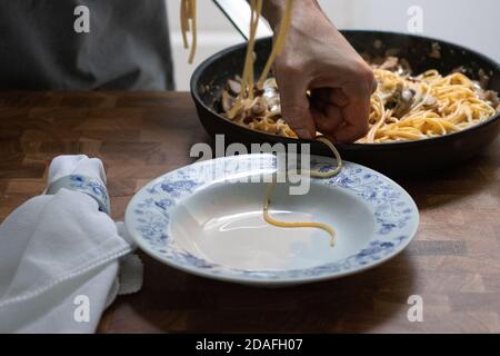 Uomo che serve spaghetti al Funghi in cucina su un tavolo di legno Foto Stock