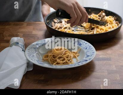 Uomo che serve spaghetti al Funghi in cucina su un tavolo di legno Foto Stock