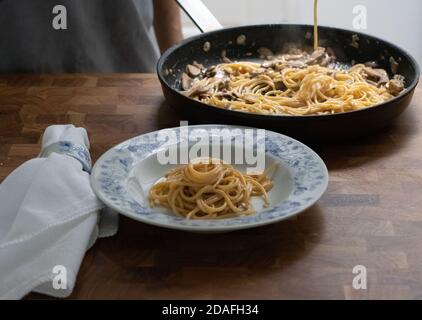 Uomo che serve spaghetti al Funghi in cucina su un tavolo di legno Foto Stock