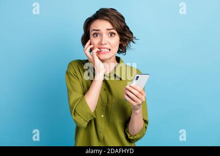 Foto di terrorizzata signora di charme capelli corti tenere telefono mani unghie morso spaventato look stressato fotocamera indossare camicia verde blu isolato Foto Stock