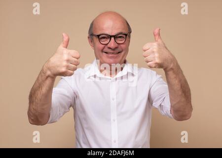 Uomo anziano allegro che dà il pollice in su approvando la vostra scelta Foto Stock