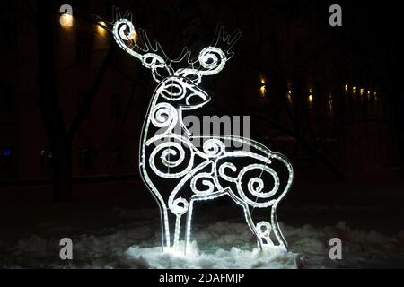 Figura di cervo da ghirlanda incandescente nella notte oscura di inverno dentro neve Foto Stock