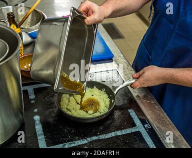 Simon Klein versa il liquido di liquirizia ridotto da un vassoio di metallo sulle cipolle sudate nella padella nella cucina della birreria Heller-Bräu Schlenkerla di birra affumicata a Bamberg, Bavaria, Germania. I tunks venivano serviti caldi e freddi nel Medioevo. Questa tunka Schlenkerla combina liquirizia di Bamberg, cipolle e majorana francica. Foto Stock